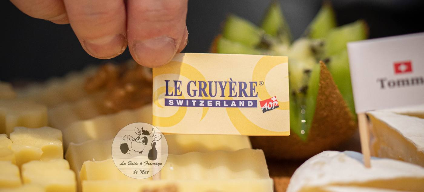 Une main pose un fanion Le Gruyère AOP sur un plateau de fromages