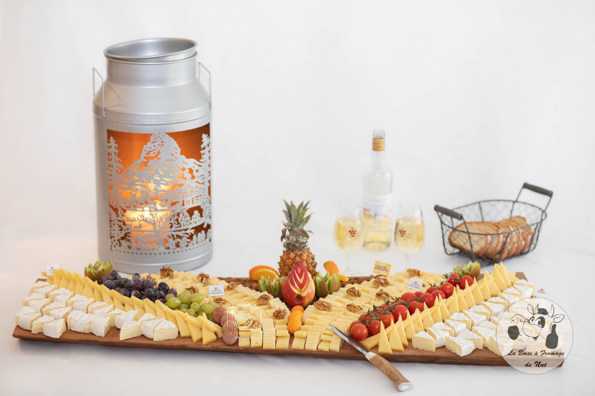 Grand plateau de fromages, fruits et noix, avec bidon à lait lumineux et verres de vin blanc